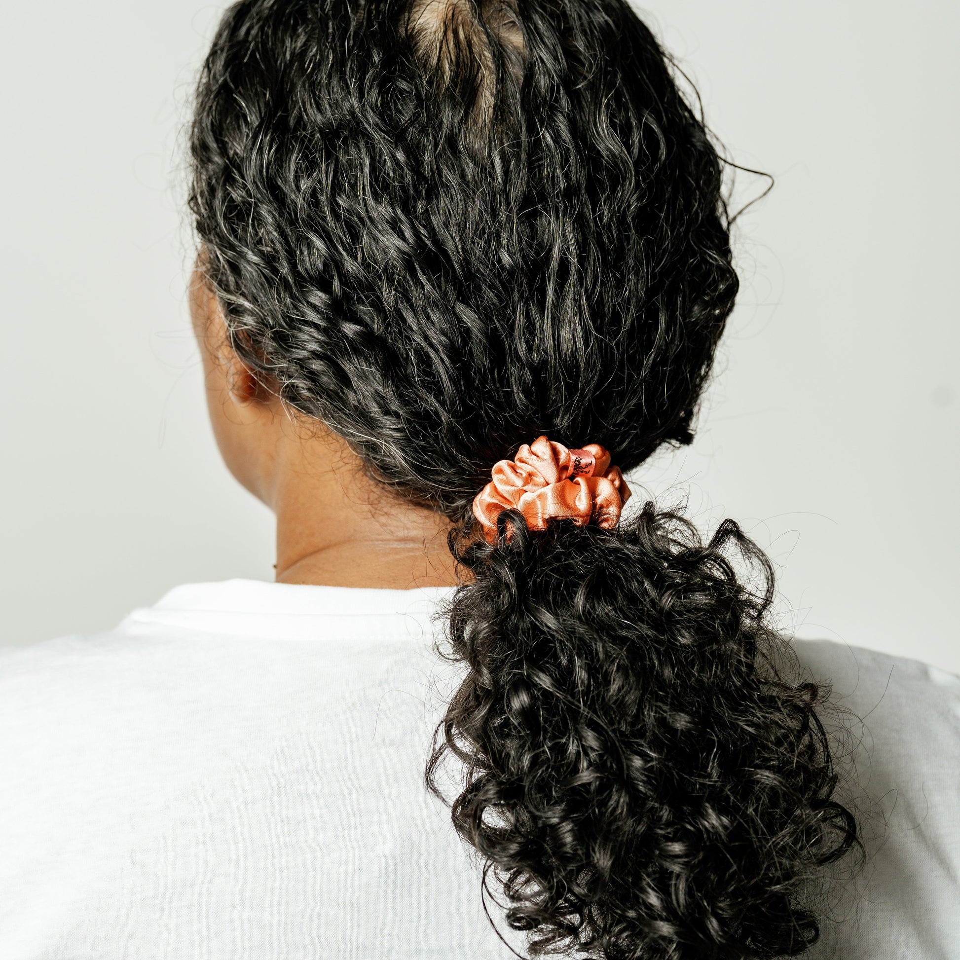 Organic silk small scrunchie in peachy coral from LINA LENNOX, showcasing its soft, glossy texture and gentle elastic band.