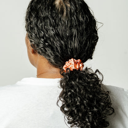Organic silk small scrunchie in peachy coral from LINA LENNOX, showcasing its soft, glossy texture and gentle elastic band.