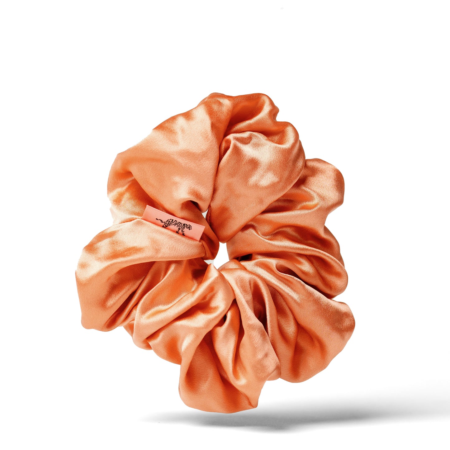 Organic silk oversized scrunchie in peachy coral by LINA LENNOX, shown in a close-up image highlighting soft, smooth fabric and stylish design.