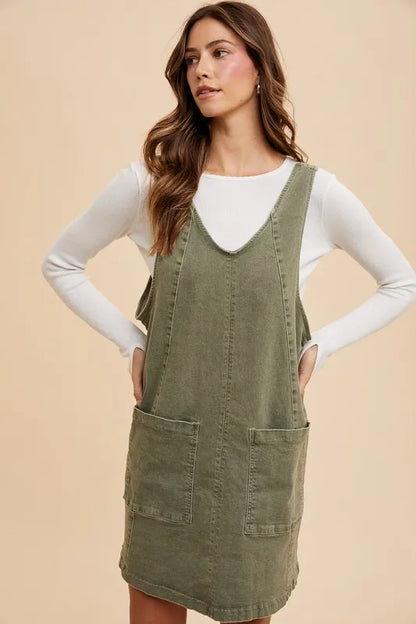 Army green Annie Wear denim overall dress with V-neck, adjustable straps, and front pockets, styled for casual wear.