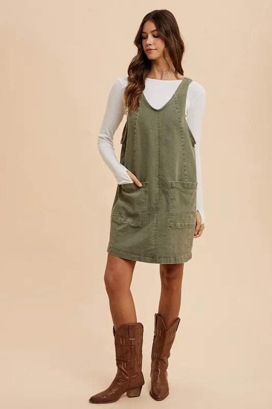 Army green Annie Wear V-neck denim overall dress with adjustable straps and front pockets, styled with casual accessories.