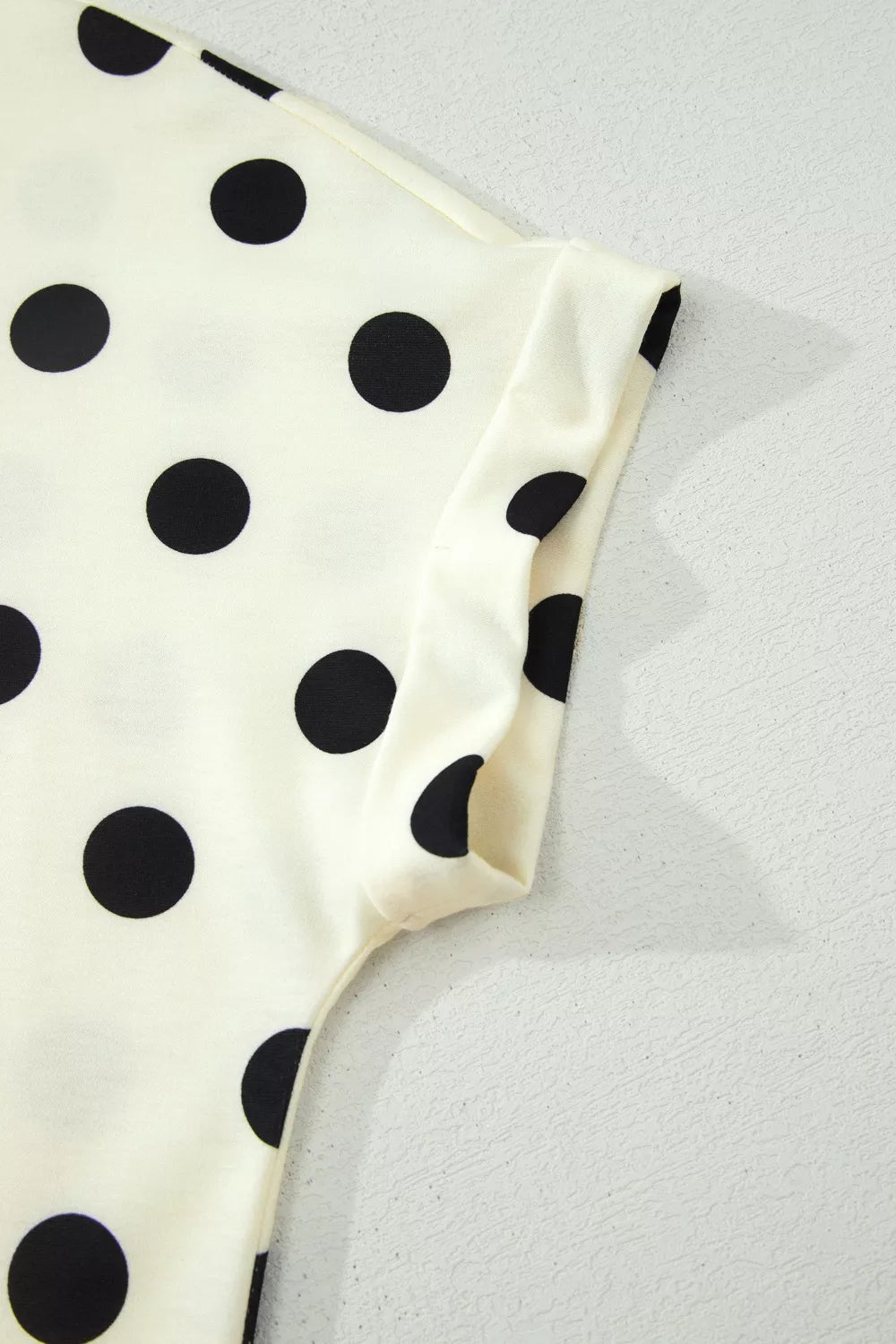 Beige polka dot mock neck short sleeve blouse from Trendsi, featuring a stylish and feminine design with a mock neckline and polka dot pattern.