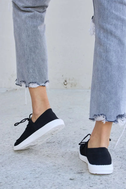 Black Forever Link flat round toe lace-up sneakers by Trendsi, shown from the side with white soles and classic sneaker design.