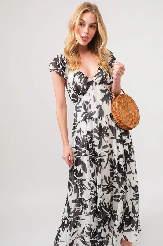 Black and cream ruffled sleeve tiered floral print maxi dress by Trendsi, featuring flowing fabric and elegant floral design.