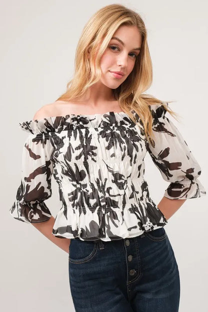 Black and cream floral printed smocked off-shoulder top by Trendsi, featuring a feminine design and floral pattern.