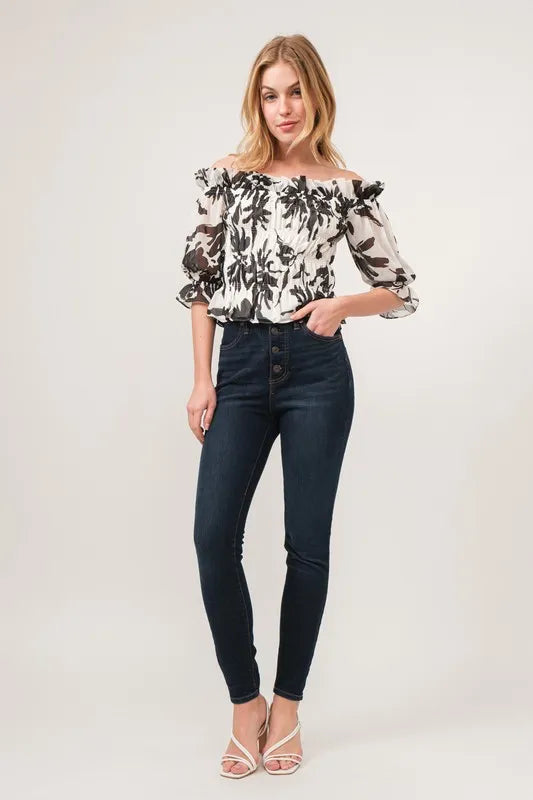 Black and cream floral printed smocked off-shoulder top by Trendsi, featuring a feminine design with ruffled details.
