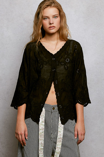 Black floral eyelet V-neck salloped shirt by Trendsi, showing detailed eyelet fabric and scalloped hem design.