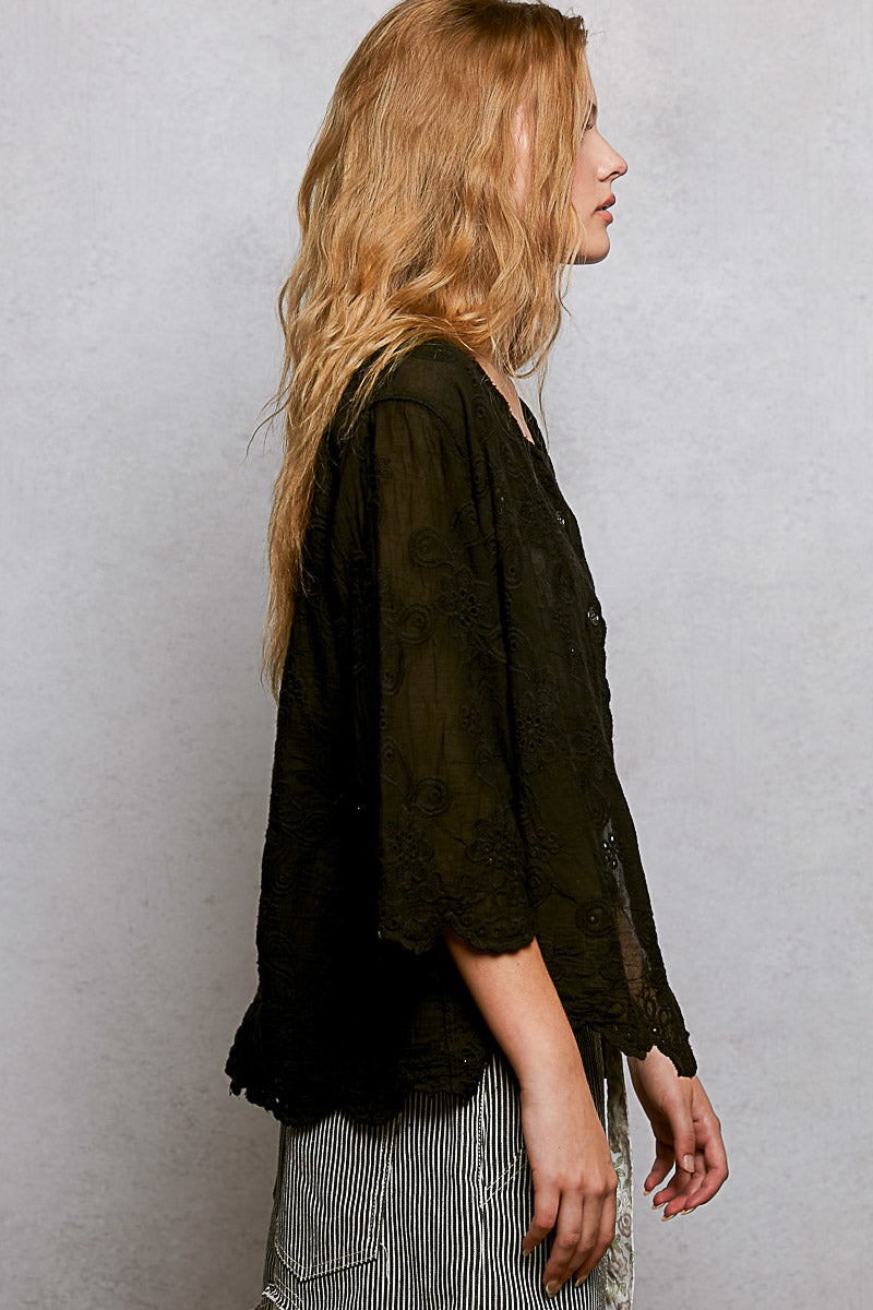 Black floral eyelet V-neck shirt with scalloped hem from Trendsi, featuring a relaxed fit and eyelet detailing.