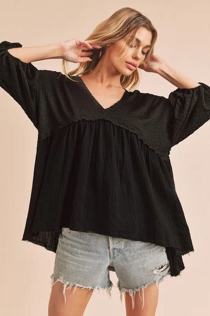 Black Aemi + Co high-low frayed hem V-neck blouse with long sleeves and relaxed fit, stylishly displayed on a hanger.