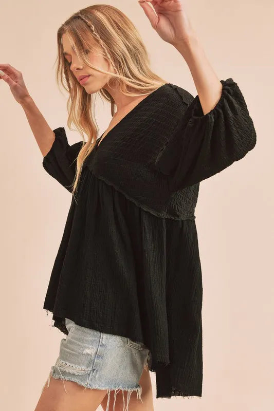 Black Aemi + Co high-low V-neck blouse with frayed hem, featuring a stylish and relaxed fit on a model.