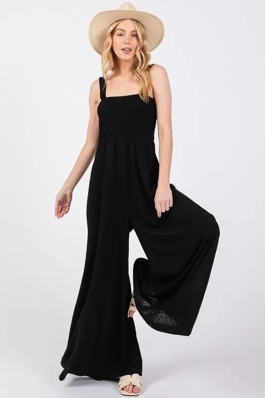 Black Sage+Fig smocked flowy wide-leg jumpsuit with relaxed fit and adjustable straps, stylish and comfortable for casual wear.
