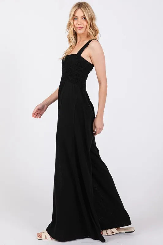 Black Sage+Fig smocked flowy wide-leg jumpsuit with relaxed fit and adjustable straps, perfect for casual or summer wear.