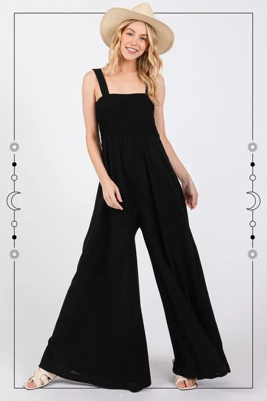 Black Sage+Fig smocked flowy wide-leg jumpsuit with adjustable straps and relaxed fit, perfect for casual or summer wear.