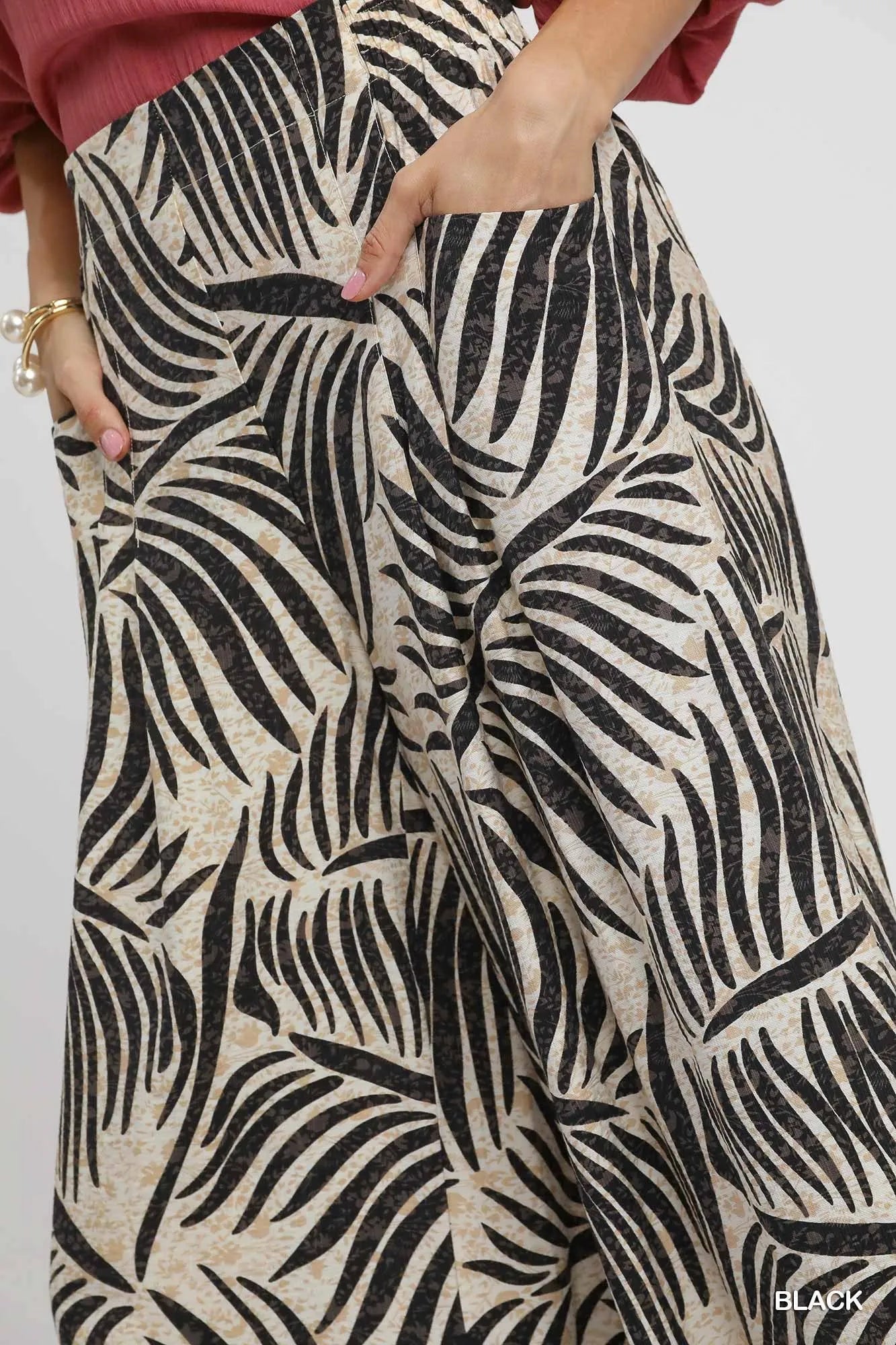Black Umgee palm leaf print wide-leg culotte pants by Trendsi, featuring a comfortable flowy fit and stylish tropical pattern.