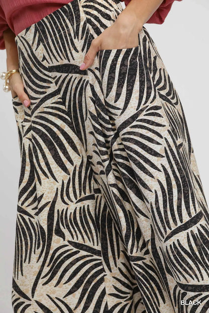 Black Umgee palm leaf print wide-leg culotte pants by Trendsi, featuring a comfortable flowy fit and stylish tropical pattern.