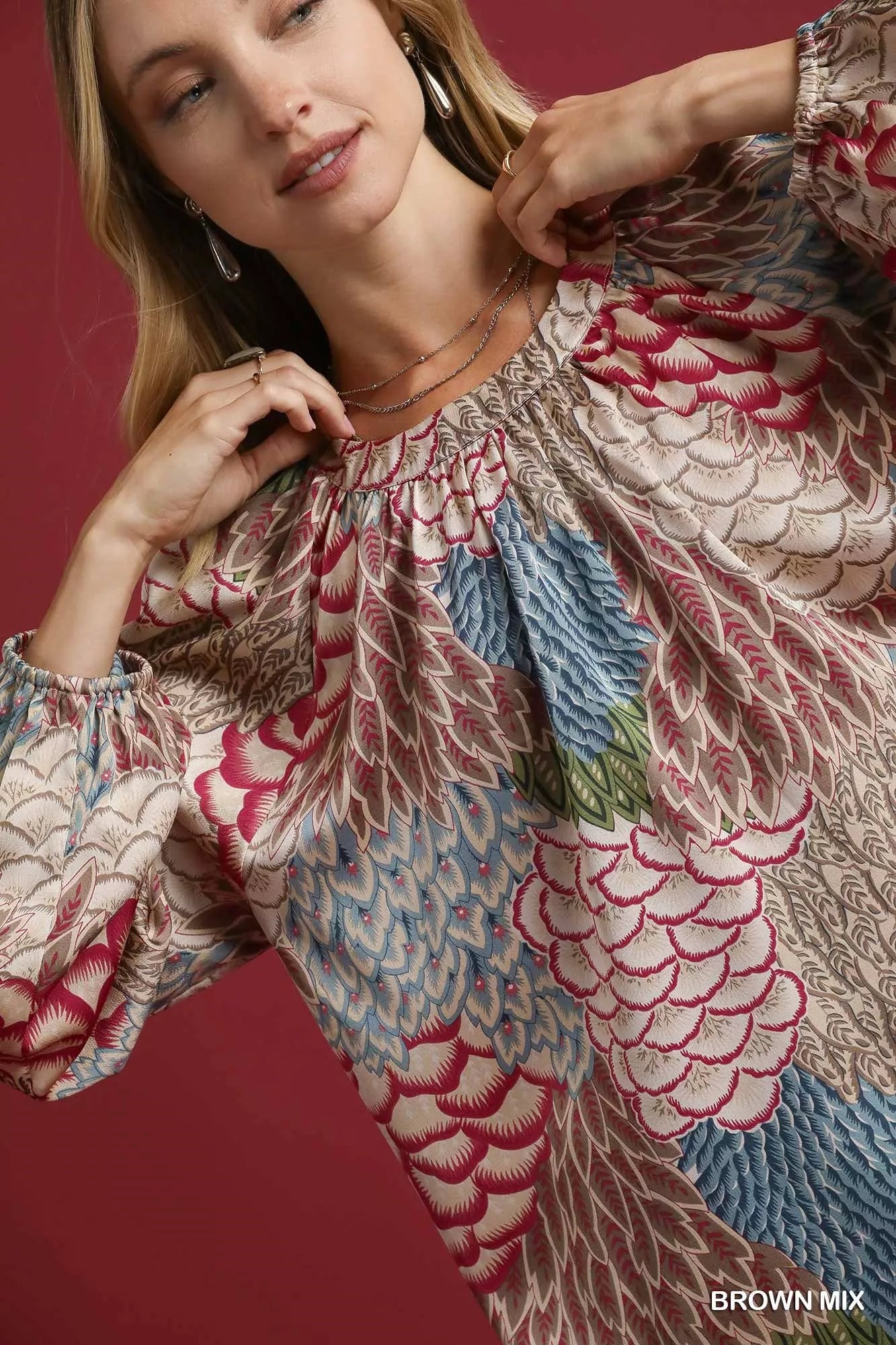 Brown Umgee boho feather print peasant blouse with long sleeves and relaxed fit, styled on a model.