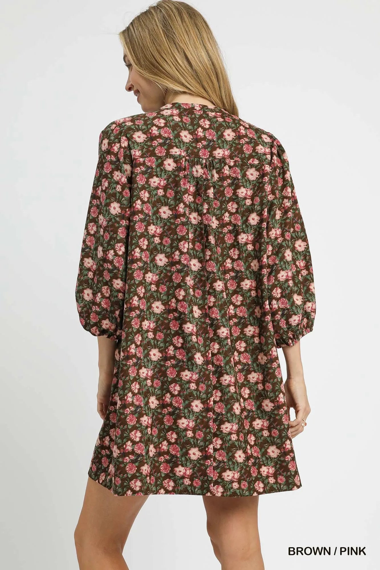 Brown and pink floral tie-neck babydoll dress by Umgee with ruffled hem, worn by a model in a casual outdoor setting.