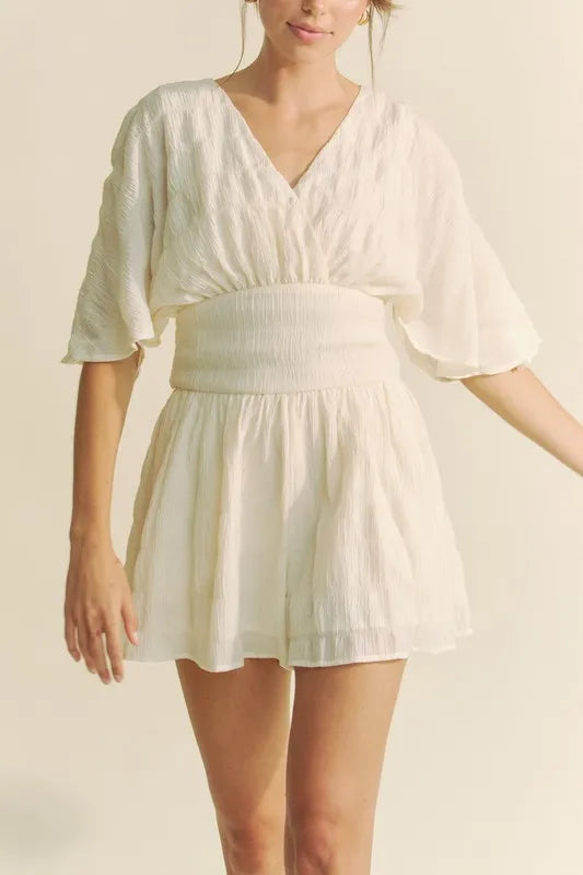 Cream Davi & Dani batwing sleeve waist belt romper by Trendsi, featuring flowy sleeves and a fitted waist.