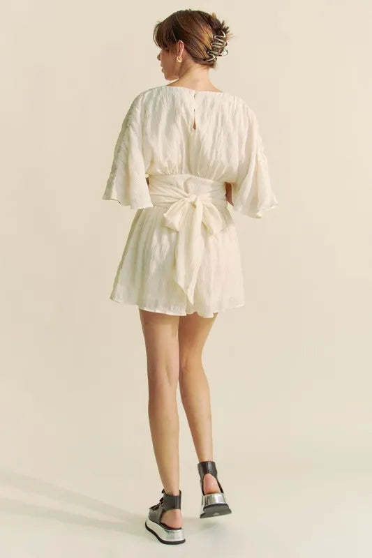 Cream Davi & Dani Batwing Sleeve Waist Belt Romper by Trendsi, featuring flowy batwing sleeves and a waist belt for a stylish look.