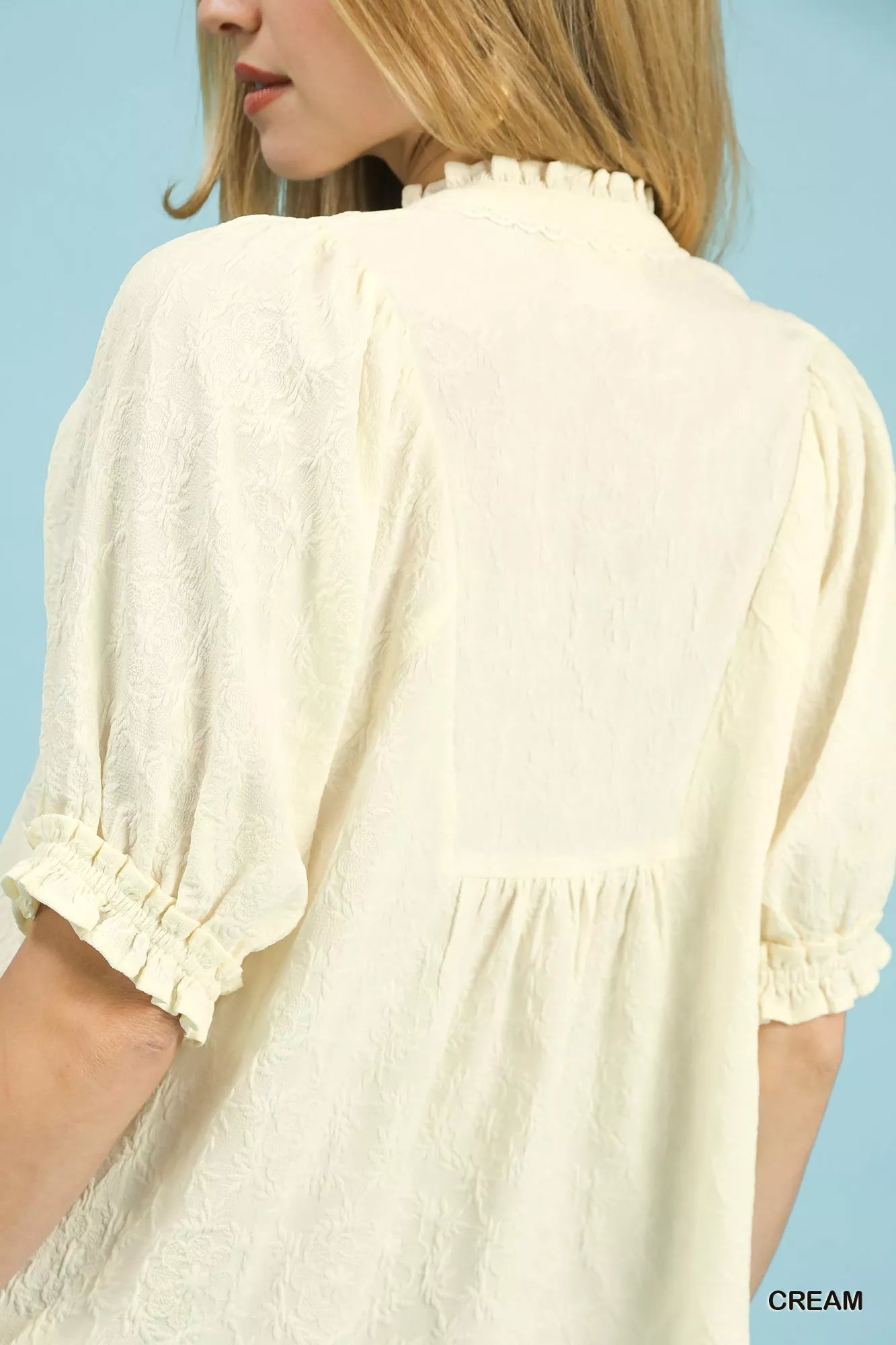 Cream textured smocked peasant top by Umgee with ruffled neckline and long sleeves, styled on a hanger.