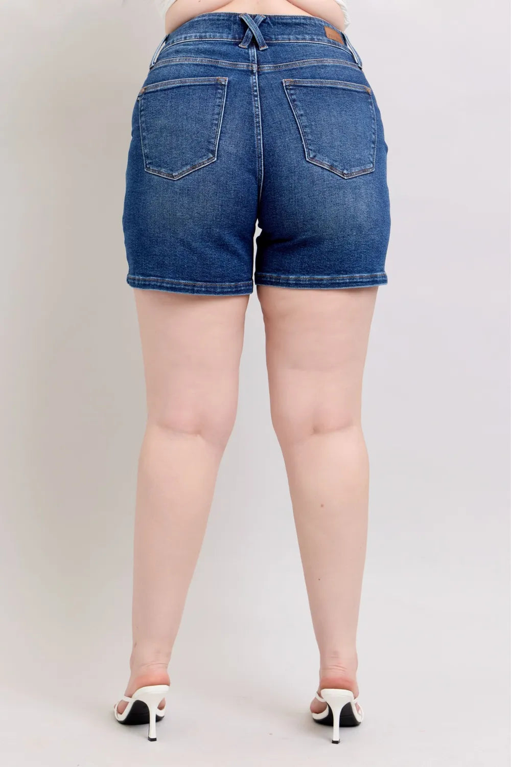 Dark blue Judy Blue plus size denim shorts with double button waistband, shown on a model. Comfortable, stylish plus size shorts.