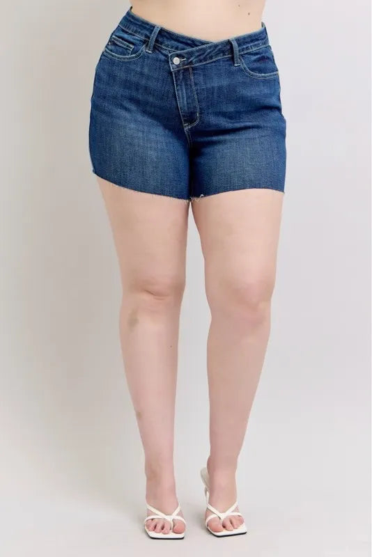 Plus size Judy Blue high waist denim shorts with criss-cross waistband, showing front view with distressed details and raw hem.
