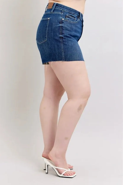 Plus size Judy Blue denim shorts with high waist and criss-cross waistband, shown on a model with casual styling.