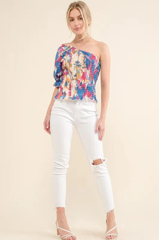 Allover floral print smocked one-shoulder blouse by Trendsi with ruffled neckline and vibrant floral pattern.