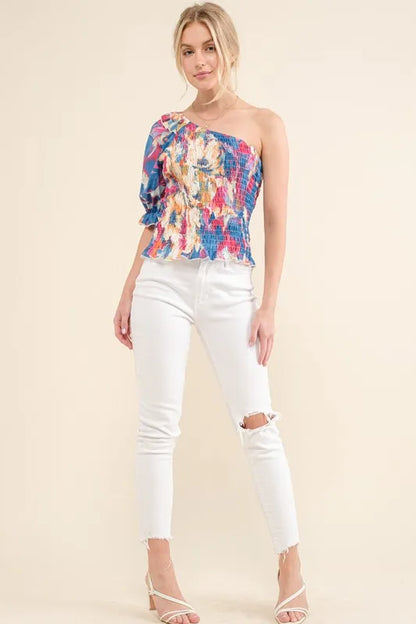 Allover floral print smocked one-shoulder blouse by Trendsi with ruffled neckline and vibrant floral pattern.