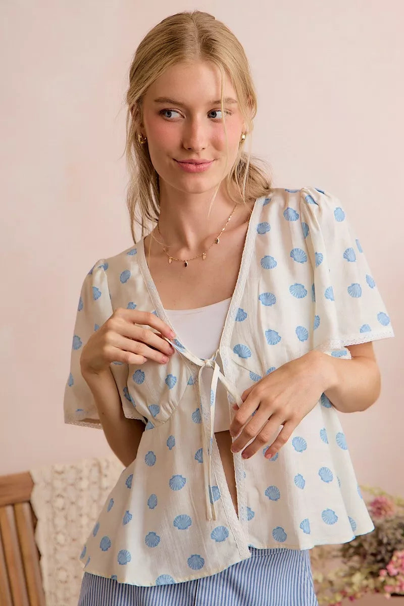 Ivory and blue SO ME Shell Print tie-front blouse with flutter sleeves, by Trendsi, shown on a model.