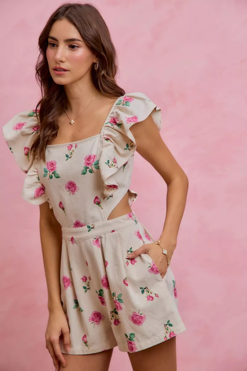 Women's floral print denim romper with cut-out waist and ruffled details, featuring a feminine, trendy design in ivory and pink.