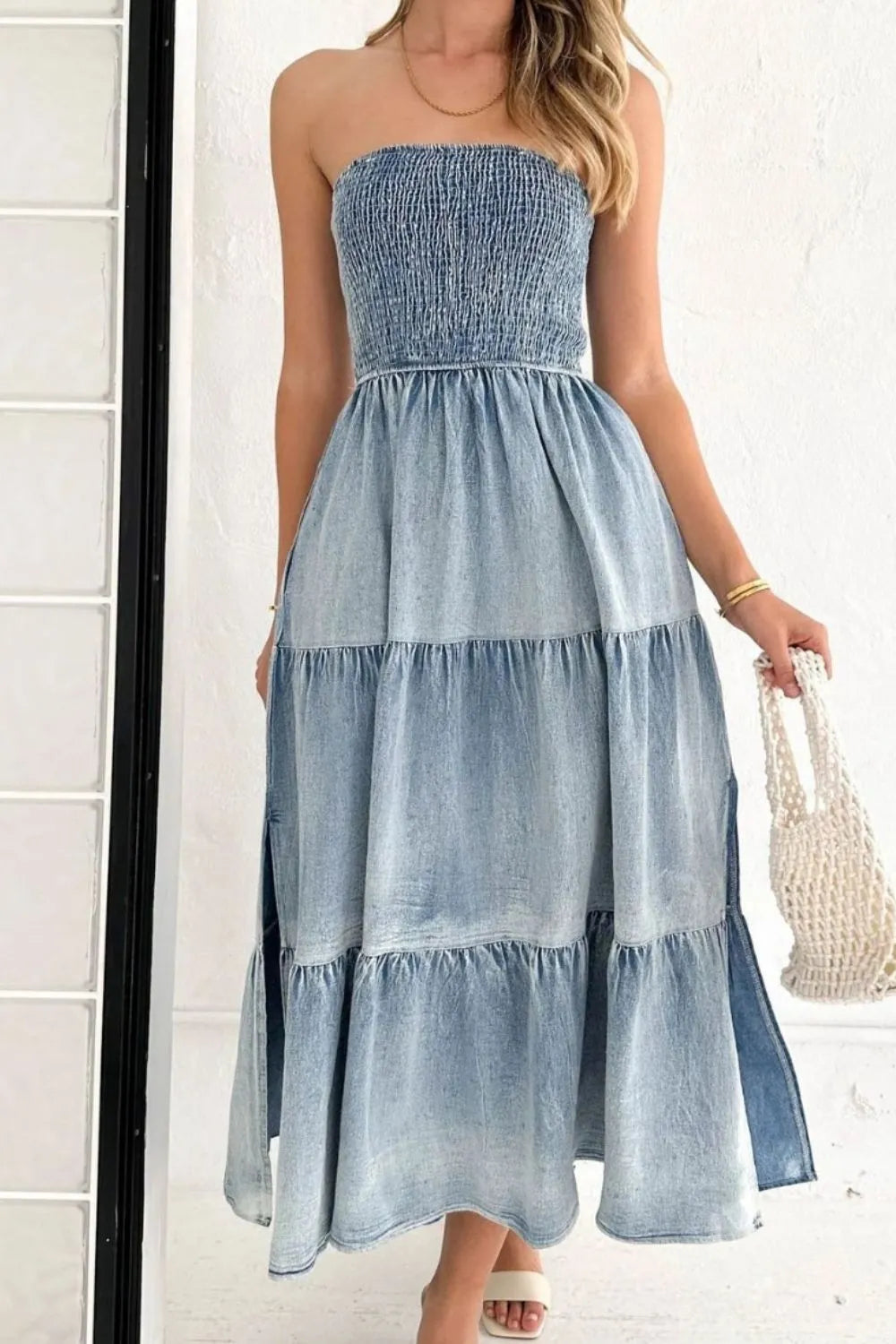Light blue smocked tube denim dress with slit and tiered design, featuring a trendy and fitted silhouette.