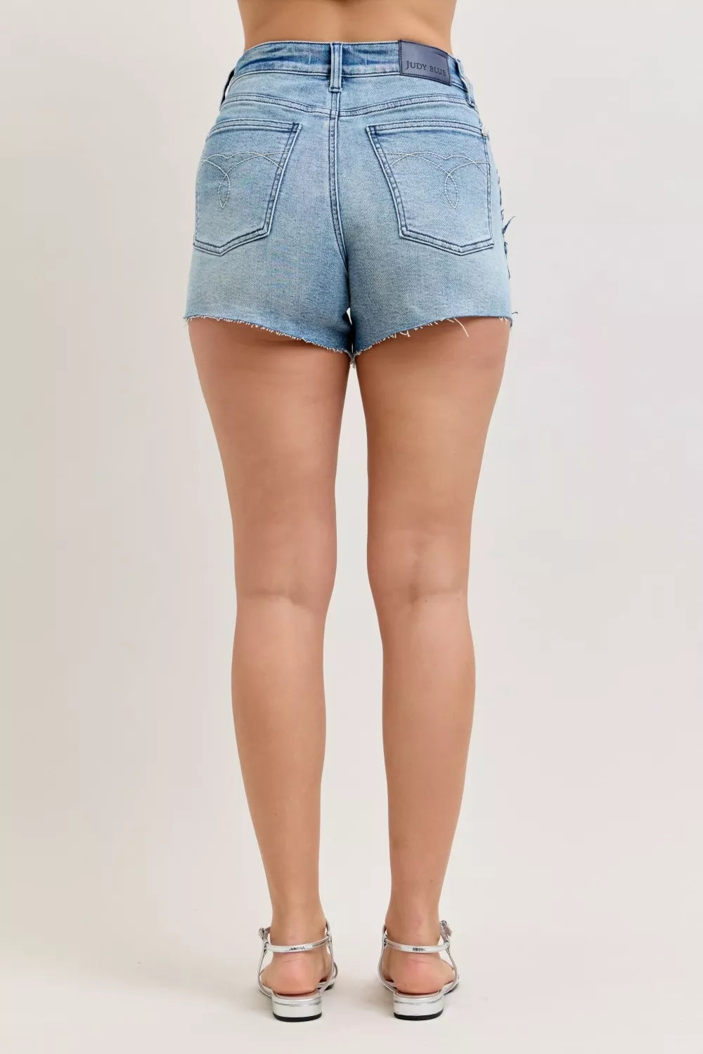 Judy Blue HW Rigid Magic Cut Off Denim Shorts with raw side seams, showcasing distressed denim and frayed edges.