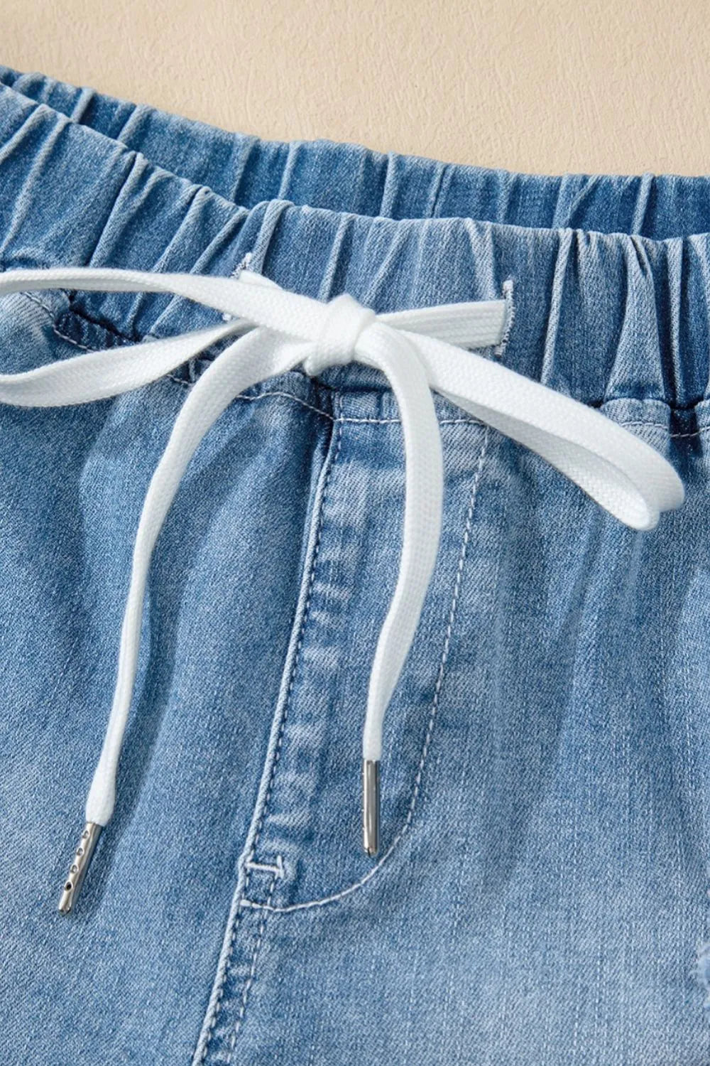 Medium-length distressed denim shorts with a drawstring waist from Trendsi, high-rise fit, casual style, and frayed hem detail.