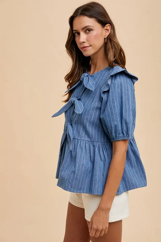 Denim peplum blouse by Annie Wear featuring a front bow and stripe details, styled with long sleeves and a fitted silhouette.