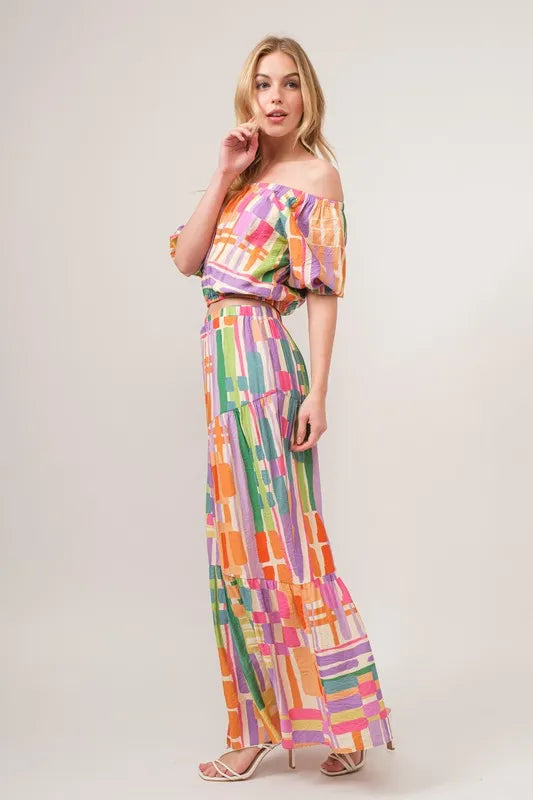 Asymmetric geo-printed tiered maxi skirt from Trendsi featuring vibrant geometric patterns and flowy fabric.
