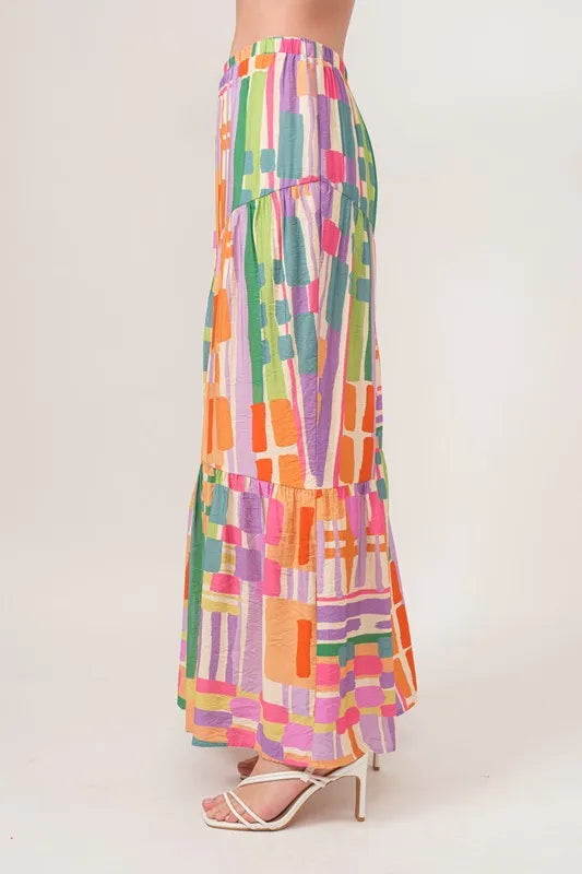 Multi-colored asymmetric geo printed tiered maxi skirt from Trendsi featuring bold geometric patterns and flowing fabric.