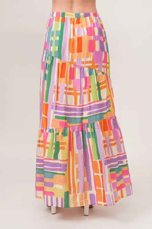 Asymmetric geo-printed tiered maxi skirt by Trendsi, featuring colorful geometric patterns and flowing fabric.