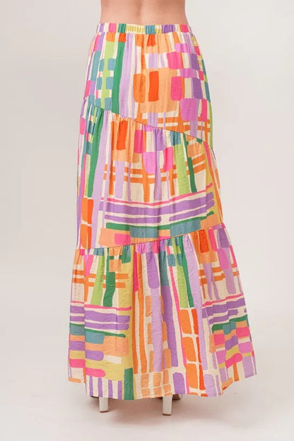 Asymmetric geo-printed tiered maxi skirt by Trendsi, featuring colorful geometric patterns and flowing fabric.