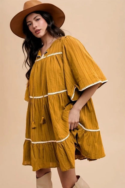 Mustard Annie Wear tiered dress with tassel contrast trim, tie-neck, and half sleeves, featuring a stylish, feminine design.