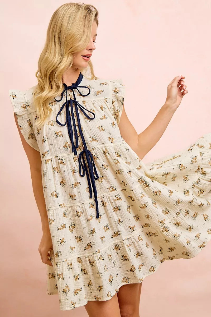 Oatmeal navy BiBi floral multi-tiered dress by Trendsi with ruffles and front tie, displayed on a hanger.