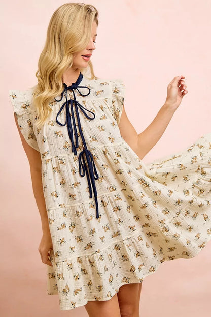 Oatmeal navy BiBi floral multi-tiered dress by Trendsi with ruffles and front tie, displayed on a hanger.
