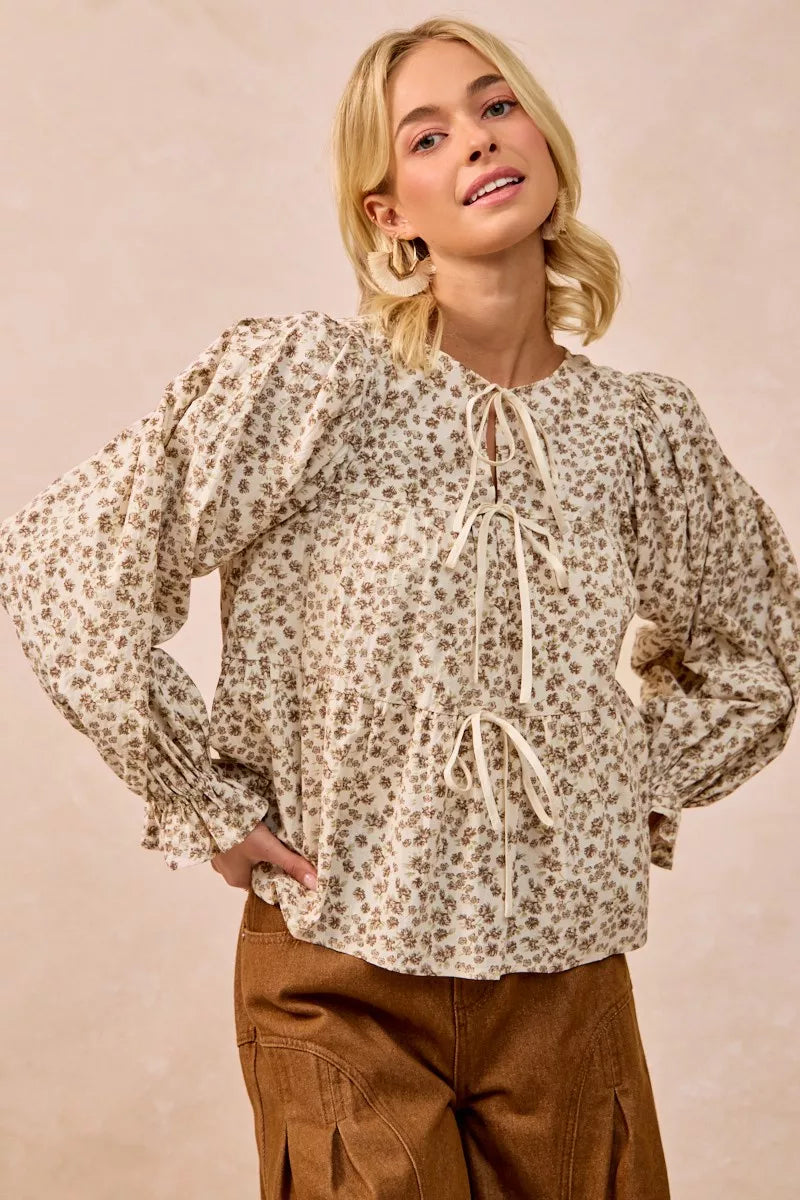 Oatmeal BiBi floral printed peplum blouse with shirring and tied front, casual fashion top by Trendsi displayed on a hanger.