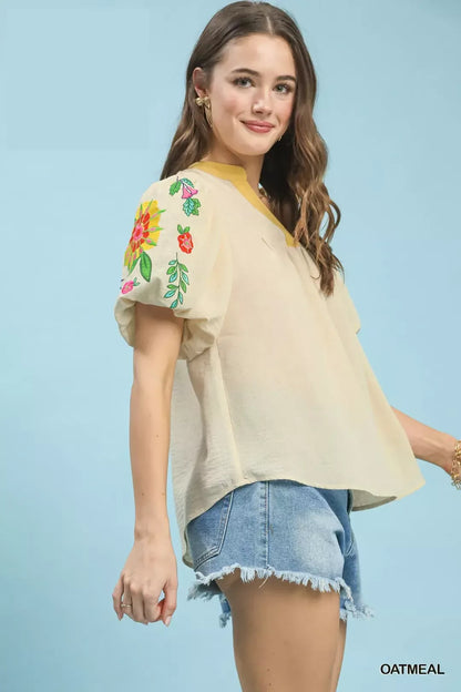 Oatmeal Umgee embroidered puff sleeve top with intricate embroidery and ruffled cuffs, displayed on a hanger.
