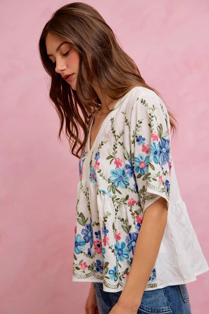 Off-white and blue floral embroidered baby doll blouse top by Trendsi, featuring delicate embroidery and a relaxed fit.