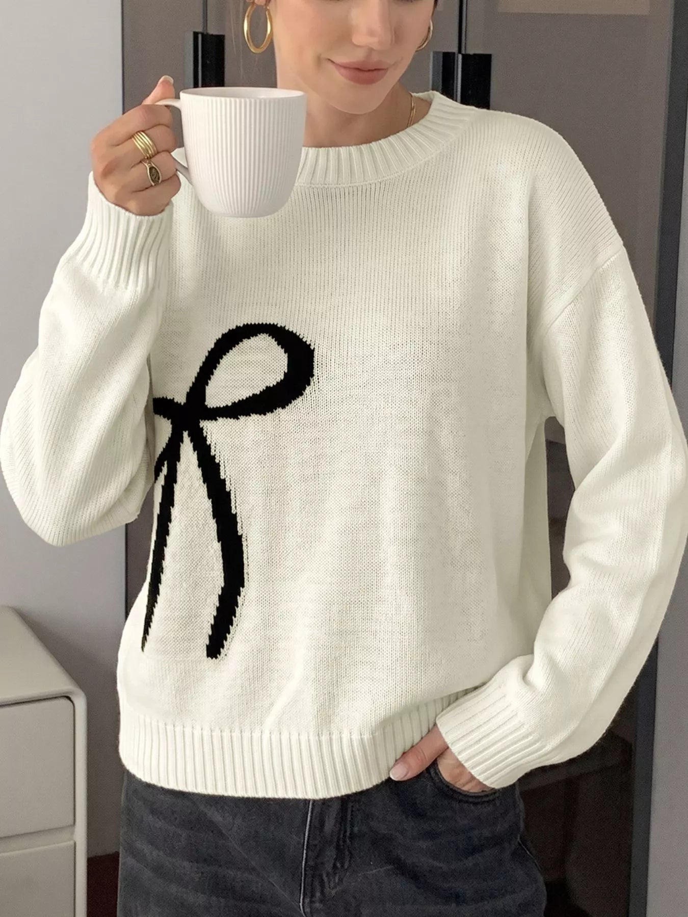Off-white Bow Graphic Round Neck Sweater by Trendsi, featuring a stylish bow graphic design on soft knit fabric.