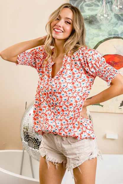 Orange floral V-neck top with smoked puff sleeves by Trendsi, featuring a stylish, feminine design and vibrant pattern.