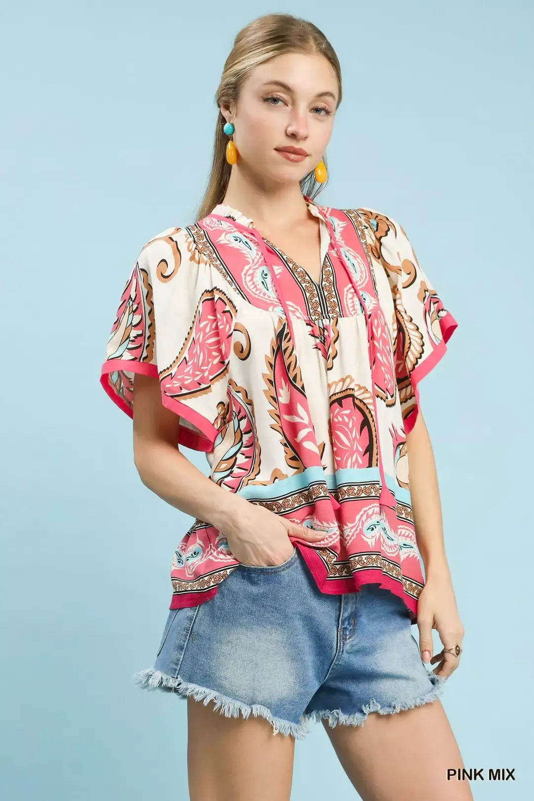 Pink Umgee tassel top with paisley border print and mixed patterns, featuring a relaxed fit and tassel details.