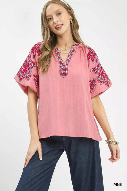 Pink Umgee embroidered sleeve top with contrast trim and relaxed fit, featuring detailed embroidery on the sleeves.