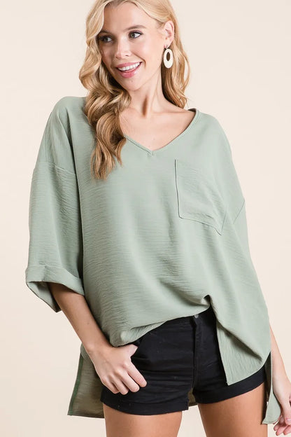 Sage green BiBi Flowy Woven V-Neck Top with rolled-up cuffs, featuring a relaxed fit and lightweight fabric, from Trendsi.